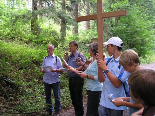 Eine Gruppe steht im Wald. Einer von ihnen hält ein großes Kreuz in der Hand.