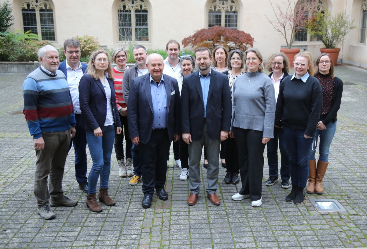 Christoph Gawronski ist aus der Abteilung Pastorale Entwicklung und Konzeption verabschiedet worden. Links von ihm Domkapitular Albin Krämer, Leiter der Hauptabteilung Seelsorge, rechts Abteilungsleiterin Christine Steger, umgeben von Kolleg:innen