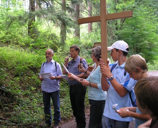 Eine Gruppe steht im Wald. Einer von ihnen hält ein großes Kreuz in der Hand.